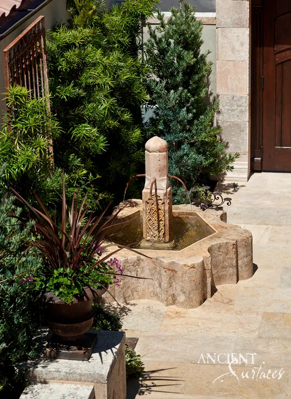 Carved antique limestone pool fountain with a scalloped basin and a fretwork column, set on limestone paving in a planted courtyard