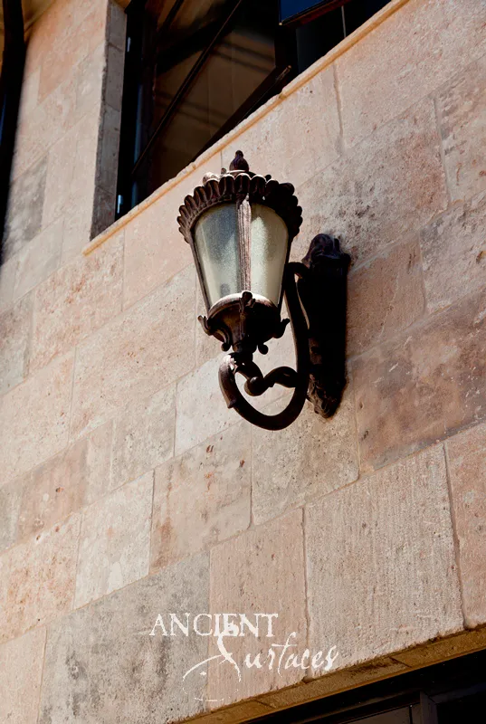 Antique limestone wall cladding in wide coursed blocks, with a wrought iron lantern mounted on the villa facade