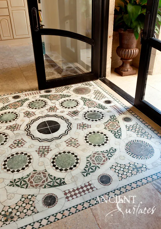 Antique stone mosaic entry floor laid in green, white and black medallions inside an iron and glass entrance door