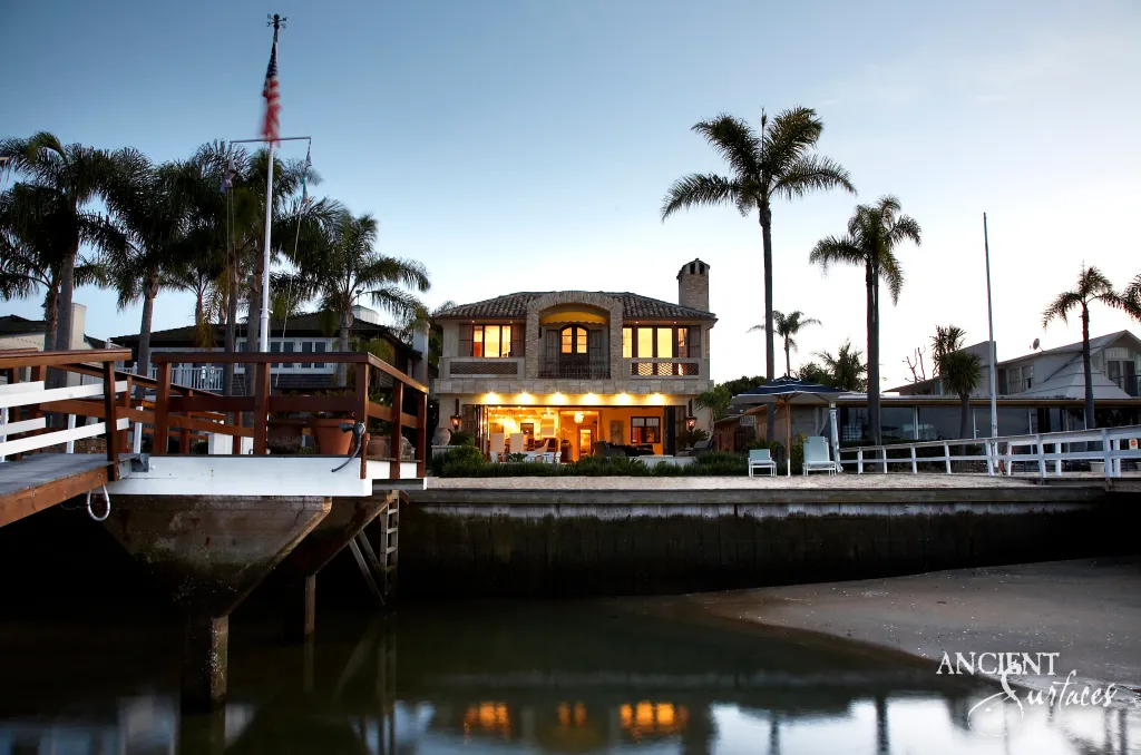 Waterfront villa clad in reclaimed limestone glowing under warm light at dusk, seen across the water