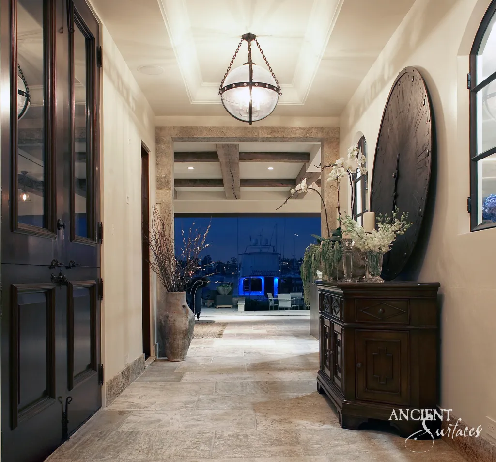 Reclaimed limestone flooring running the length of a hallway past a carved stone door surround to a lit terrace