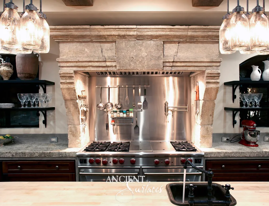 Antique limestone range hood carried on carved stone corbels above a professional range and pale stone countertops