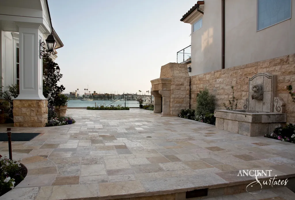 Reclaimed limestone terrace paved in a French pattern at golden hour, with a carved stone wall fountain and limestone garden walls above the water