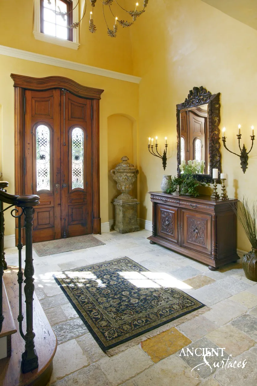 Antique biblical stone flagstone flooring in a double height entrance hall beneath carved wood entry doors