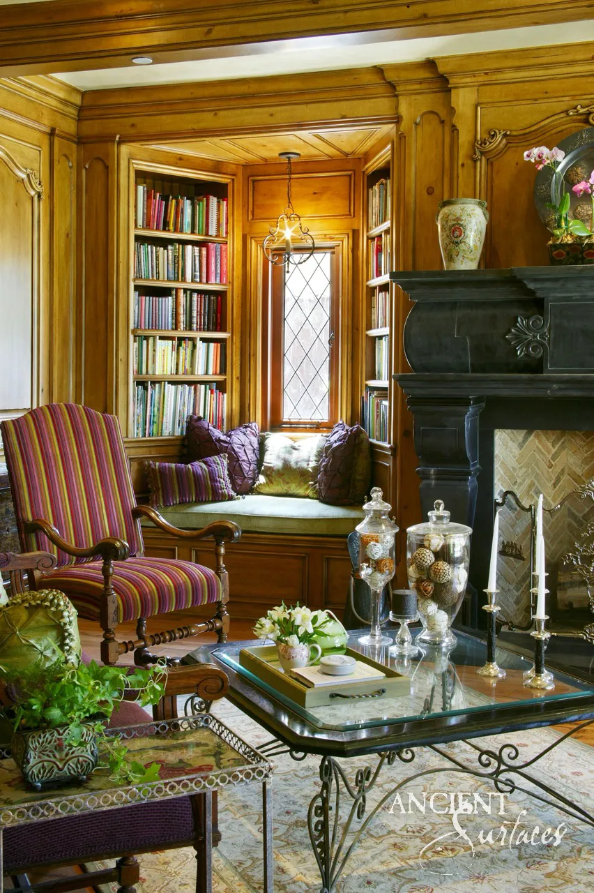 Carved antique black marble fireplace mantel above a herringbone firebox in a wood paneled reading nook