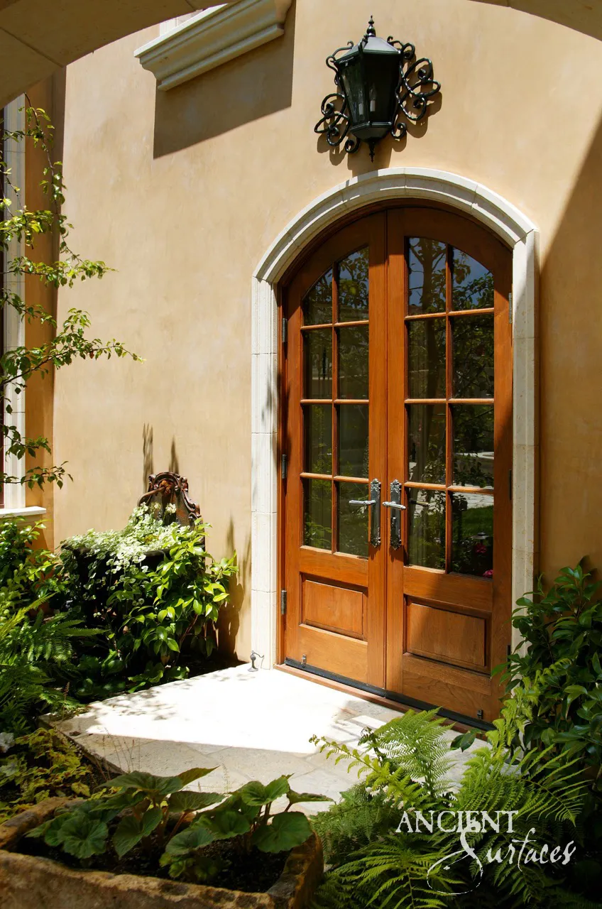 Arched entry doorway framed in carved limestone, with a limestone threshold and paving set among ferns
