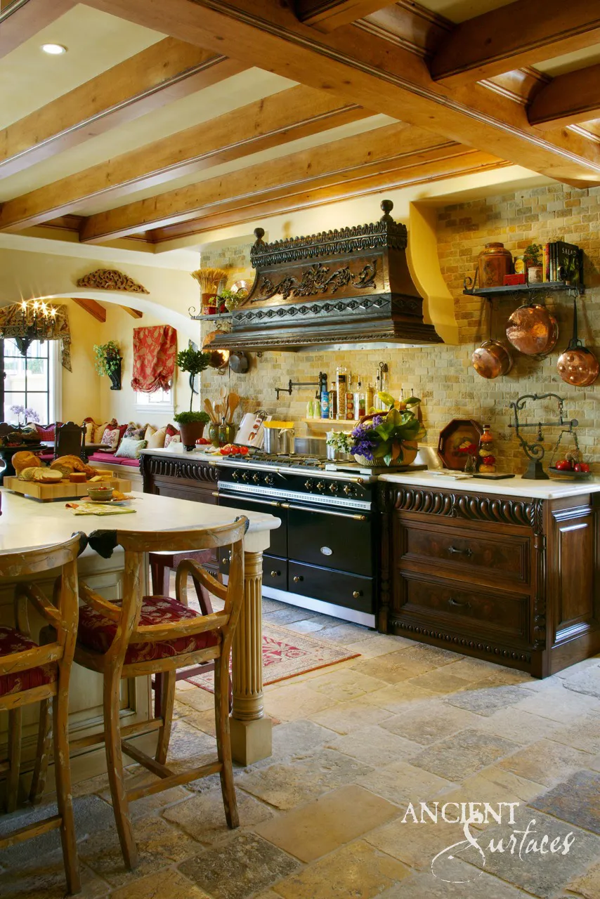Antique biblical stone kitchen floor beneath a wall of limestone brick rising to the ceiling, pale stone countertops and a carved wood range hood