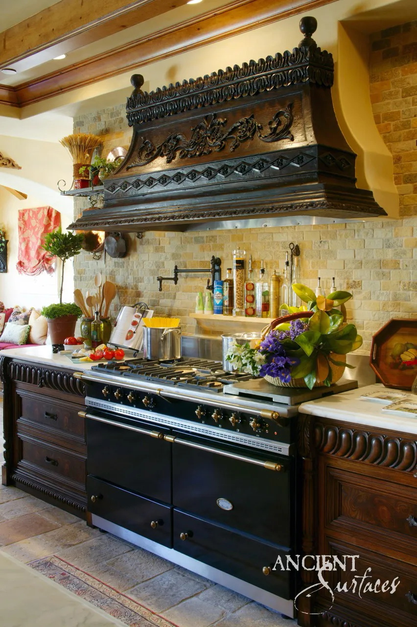 Hand-carved wood range hood worked with acanthus scrollwork above a running bond wall of pale limestone brick and a stone counter